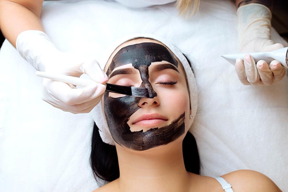 cosmetologist applying black mask pretty woman face wearing black gloves gorgeous woman spa